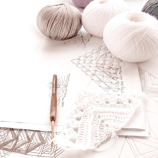 Balls of yarn, a crochet hook, and hand-drawn stitch charts on a table